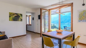 A modern dining area with a wooden table and yellow chairs, a large window with a view of a balcony, and a map on the wall. - Wonderful private villa for 5 guests with pool, WIFI, TV and patio (Bellano)