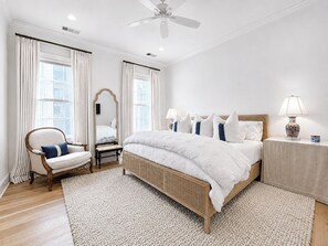 A bedroom with a large bed, a chair, a bedside table, a mirror, and a ceiling fan.