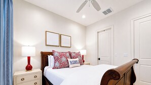 A bedroom with a wooden bed, two bedside tables, a nightstand, a red lamp, a white door, and a ceiling fan. - The Nola, 3BR Luxe Stay by Velvet Ditch Villas (Oxford)