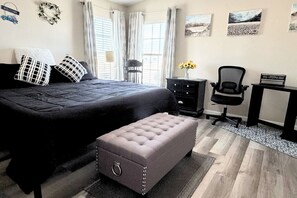 A bedroom with a large bed, a desk, a chair, and a small bench.