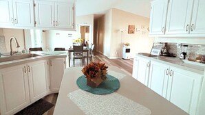Une cuisine moderne avec des meubles blancs, un îlot central agrémenté d’un vase décoratif et un coin repas avec des chaises et une table.