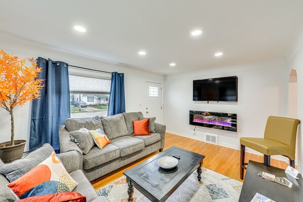 A modern living room with a grey sofa, orange cushions, a black coffee table, a potted plant, and a flat-screen TV mounted on the wall. - 'The Maple Tree' Home: 14 Mi to Downtown Cleveland (Maple Heights)
