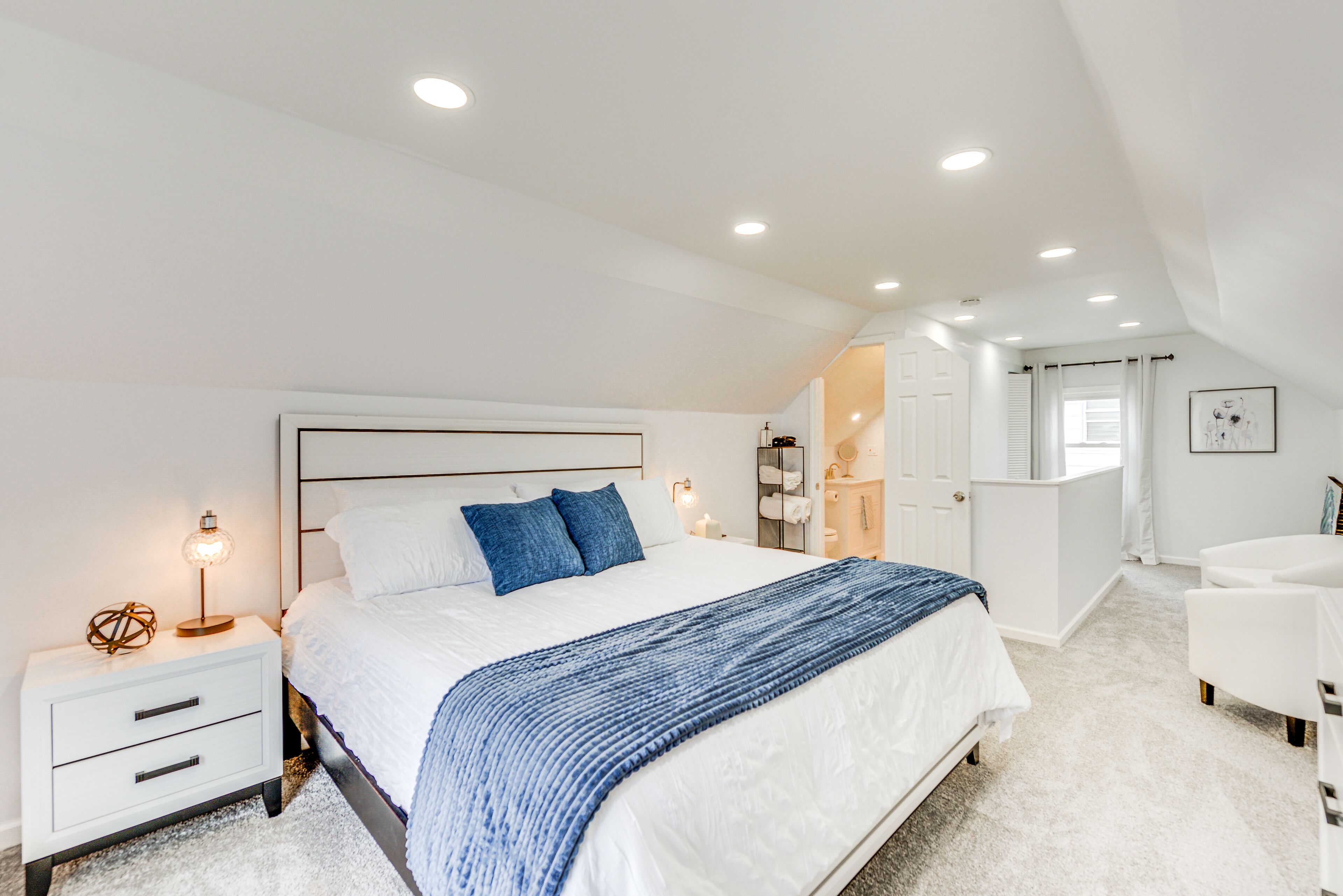 Une chambre moderne avec un grand lit, des tables de chevet blanches, une lampe de chevet et un plaid bleu.