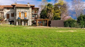 A stone house with a balcony, a wooden deck, and a fenced yard.