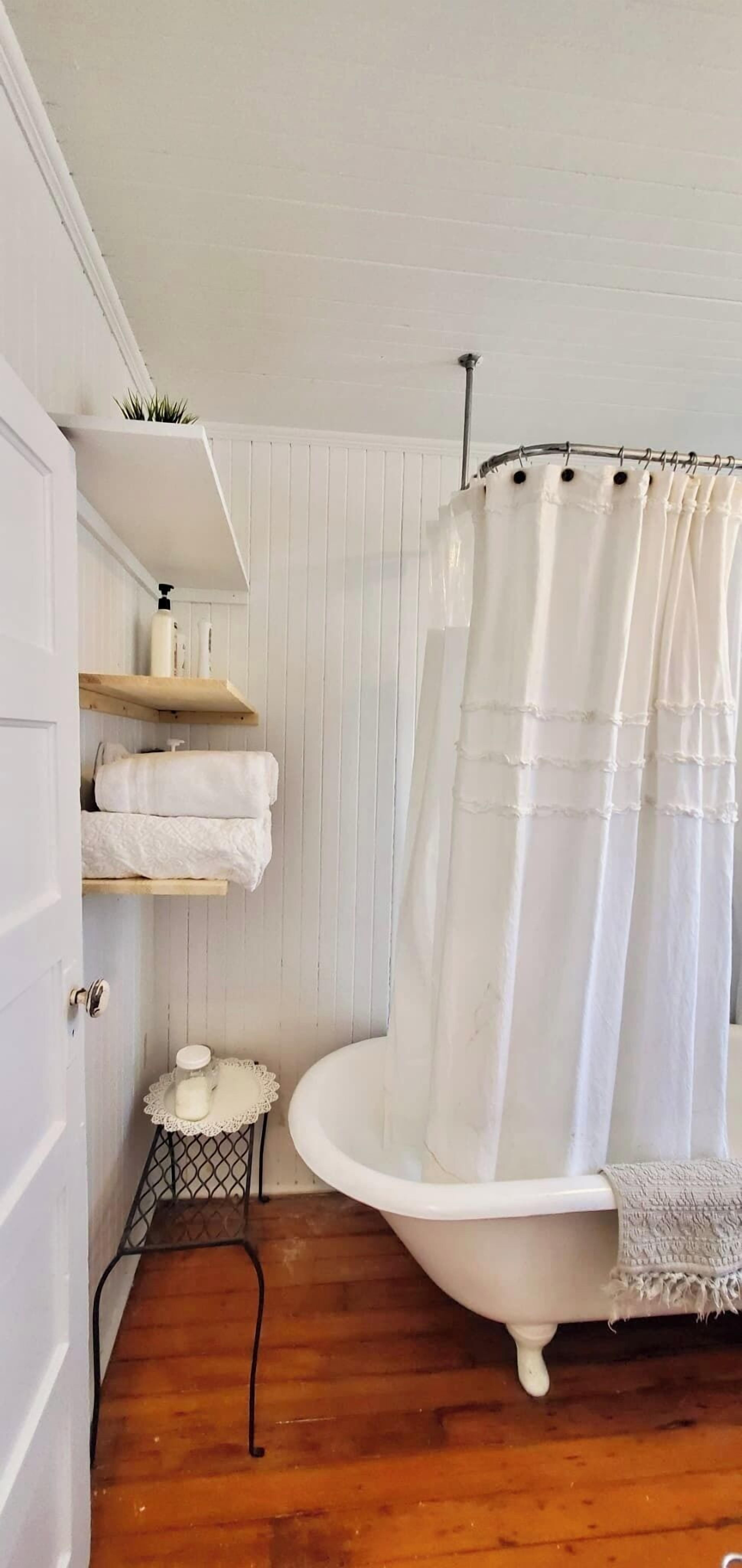 Een badkamer met een wit bad, houten planken en een witte deur.