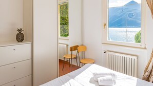 A bedroom with a bed, a chair, a small table, a radiator, and a window with a view of a mountain and water. - Lovely apartment for 4 guests with WIFI and TV (Vignola)