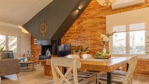 A modern living room with a fireplace, a dining area with a wooden table and chairs, and a TV mounted on the wall.