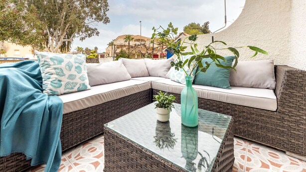 Un área de estar moderna al aire libre con un sofá de mimbre, una mesa de centro de vidrio y una planta en maceta.