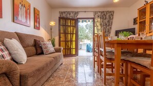 Un salón acogedor con un sofá marrón, una mesa de comedor de madera y un ventanal de vidrio que da a un espacio exterior.