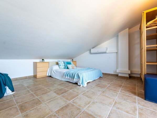 A bedroom with a bed, a wooden nightstand, a wall-mounted air conditioner, and a wooden shelf unit.