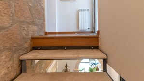 Een stenen muur, een houten bankje, een radiator en een ingelijst schilderij aan de muur.
