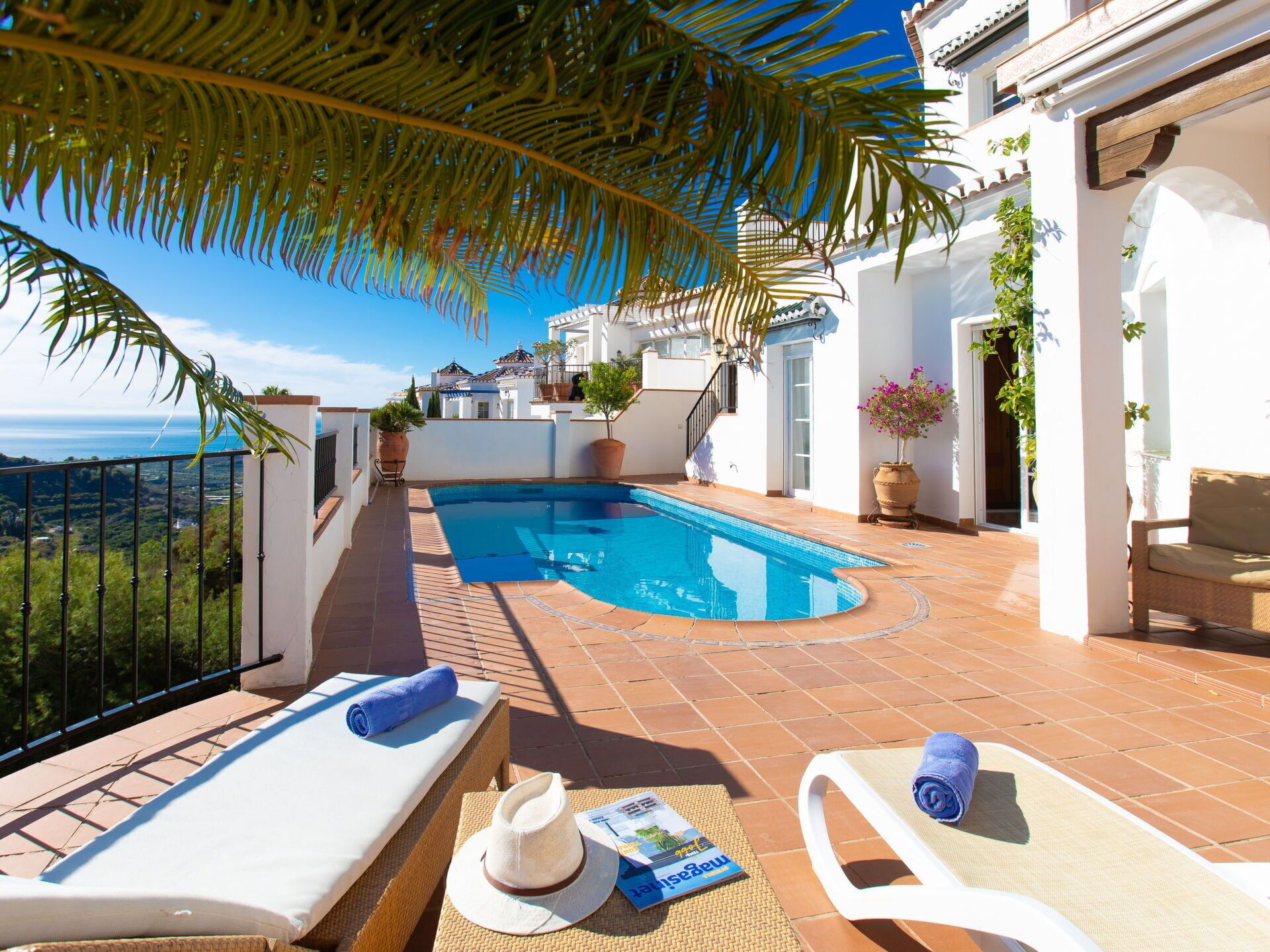 Un área de piscina en la azotea con sillones de descanso, una cama sol y vista al mar.