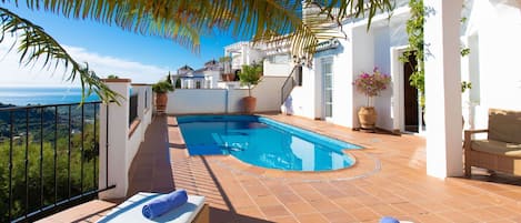 Un área de piscina en la azotea con sillones de descanso, una cama sol y vista al mar.