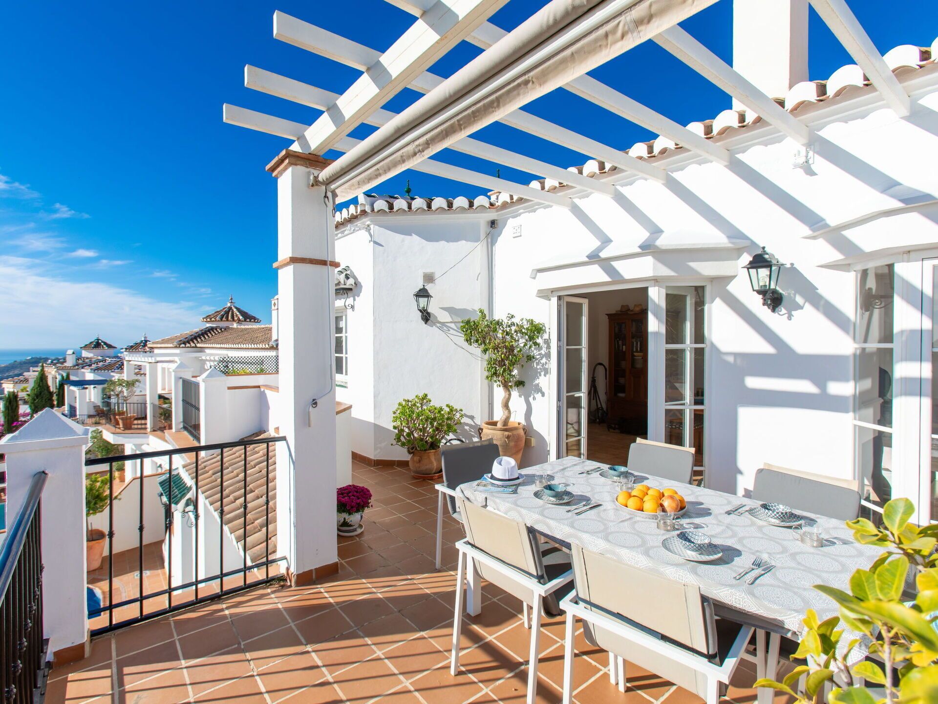 A terrace with a table set for dining, potted plants, and a view of the surrounding neighborhood.