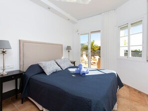 Un dormitorio con cama, dos mesitas de noche, una mesilla auxiliar, una ventana y vistas al exterior.