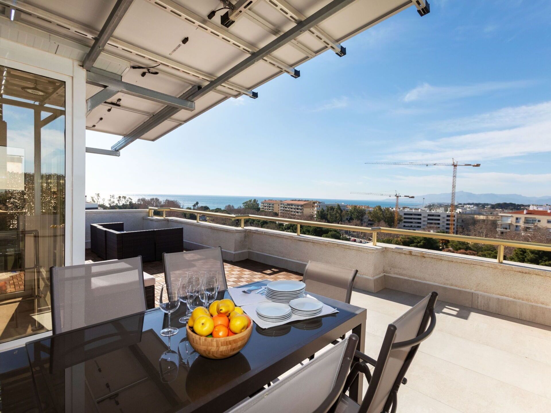 A balcony with a glass table, chairs, and a bowl of fruit.