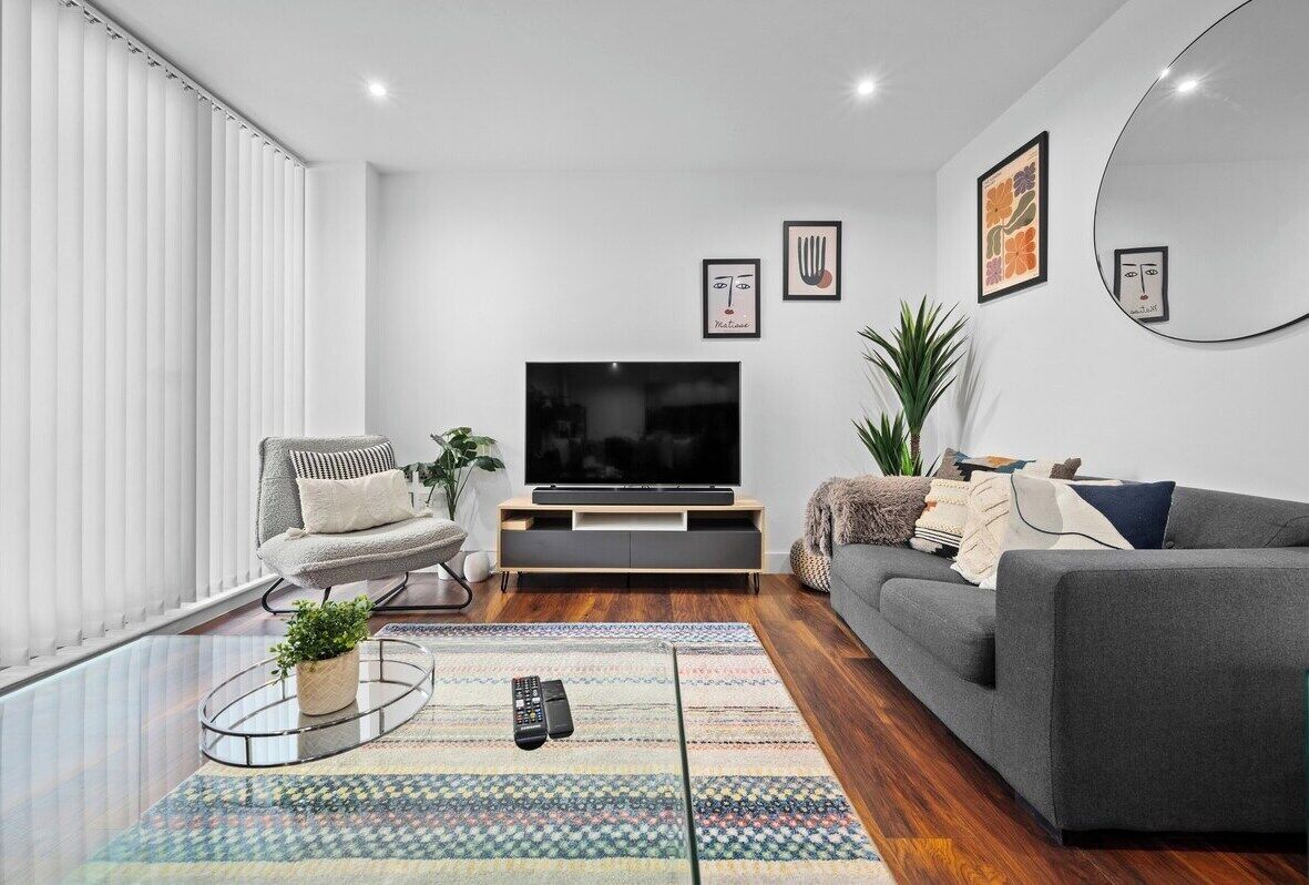 Ein modernes Wohnzimmer mit Flachbildfernseher, grauen Sofas, einem Couchtisch und einem gemusterten Teppich.