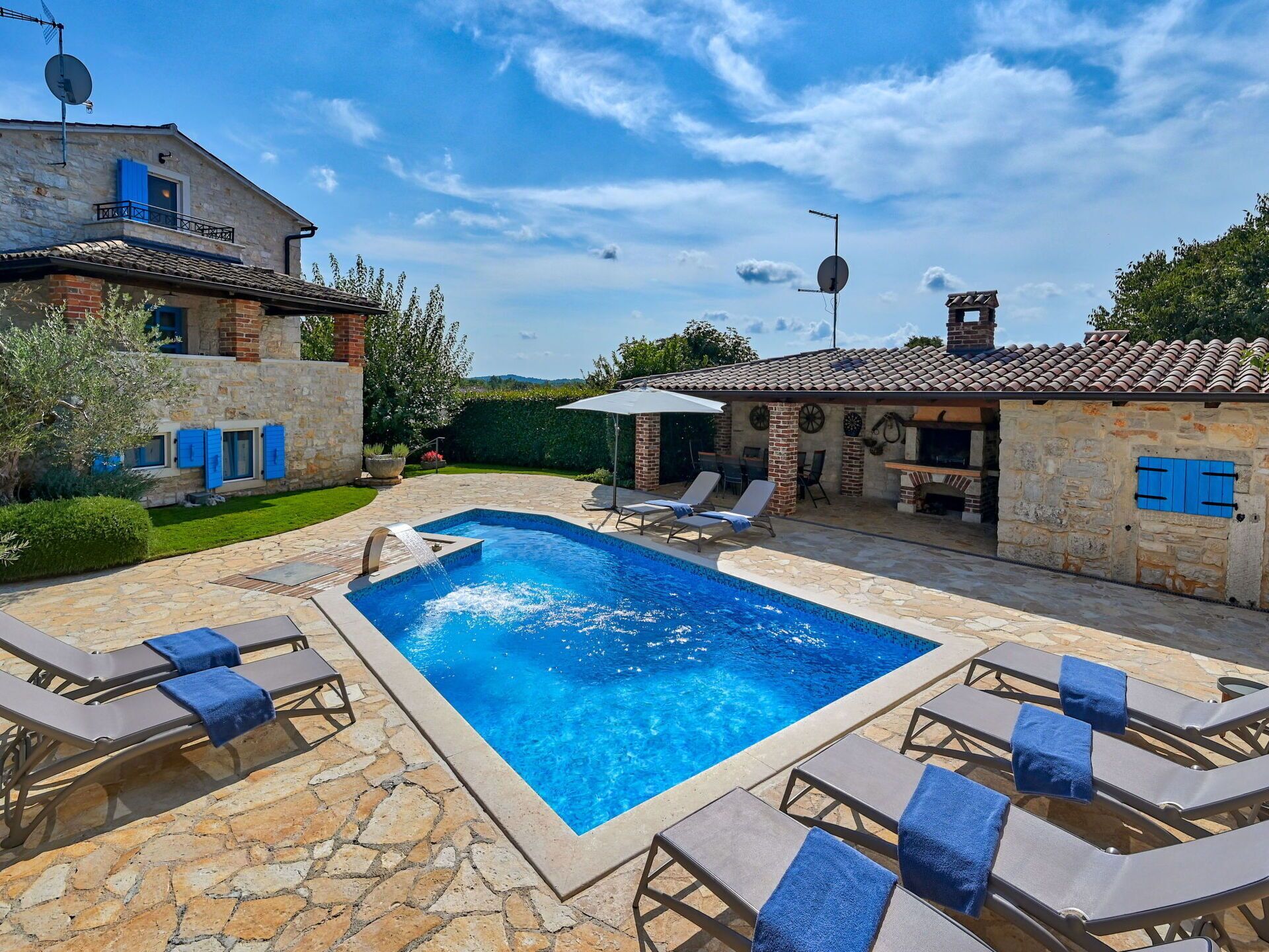 A swimming pool with lounge chairs and a barbecue area, surrounded by stone buildings and a clear sky.