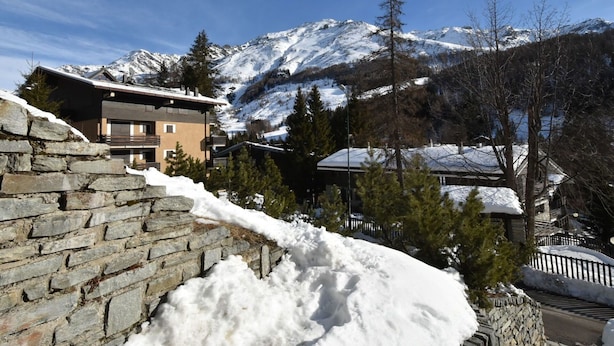 A snow-covered mountain landscape with a modern building featuring balconies and a stone wall. - Lovely apartment for 5 people with WIFI, TV and terrace (Madesimo)