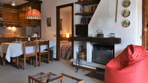 A cozy living room with a fireplace, a dining area with a table and chairs, and a kitchen with wooden cabinets and a hanging light fixture. - Lovely apartment for 5 people with WIFI, TV and terrace (Madesimo)