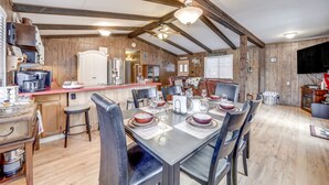 A rustic dining area with a wooden table set for four, surrounded by chairs. A kitchen area with a refrigerator and a coffee maker is visible to the left. - 2 Fire Pits & Covered Deck: Cabin in Happy Jack! (Happy Jack)