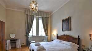 Une chambre d’hôtel avec un grand lit, un lustre, un tableau au mur et un bureau avec un miroir.