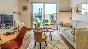 Ett modernt vardagsrum med en soffa, ett matbord med stolar, en tv och ett stort fönster med utsikt över omgivningen.