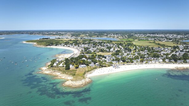 Ett flygbildsbild av en kuststad med en strand, klart blått vatten och bostadsområden.