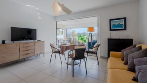 A modern living room with a flat-screen TV, a dining table with chairs, a sofa, and a balcony with a view. - Lovely apartment for 4 people with pool, WIFI, A/C, TV and terrace (Saint-cyprien-plage)