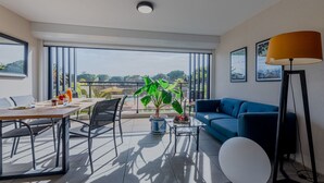 A modern living room with a balcony, a dining area, and a large window offering a view of a pool and greenery. - Lovely apartment for 4 people with pool, WIFI, A/C, TV and terrace (Saint-cyprien-plage)