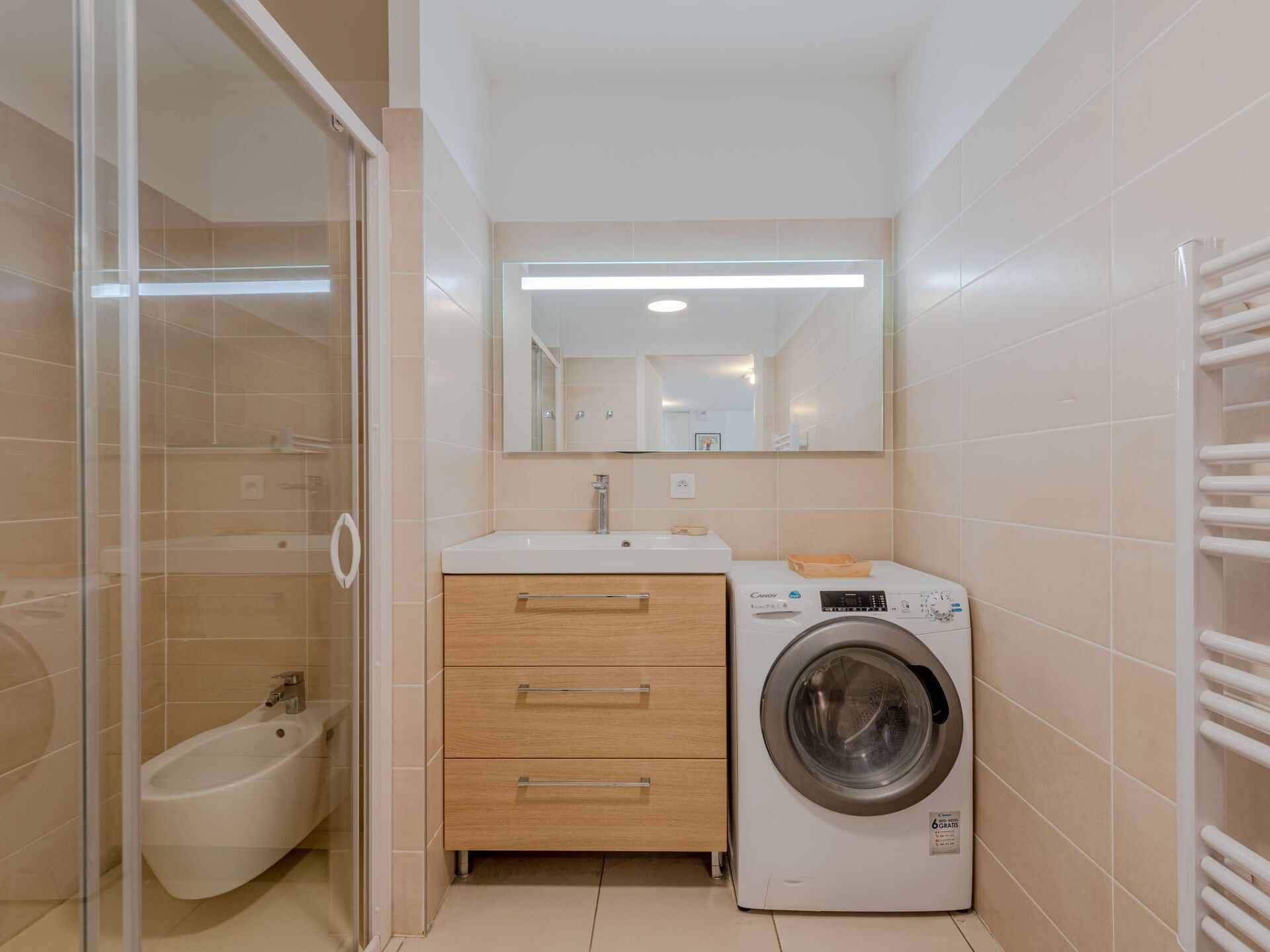 A compact bathroom with a bidet, a washing machine, and a mirror above the sink.