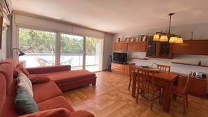 A modern living room with a red sofa, a dining area with wooden furniture, and a kitchen with wooden cabinets and a TV. - Beautiful apartment for 6 guests with A/C, WIFI, TV and terrace (Castell-platja D'aro)