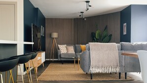 A modern living room with a grey sofa, a coffee table, and a floor lamp. There is a herringbone-patterned rug on the floor. - Luxe Penthouse Retreat: With Free Parking! (London)