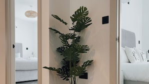 A hallway with a potted plant, a woven rug, and a bed with white bedding in the background. - Luxe Penthouse Retreat: With Free Parking! (London)