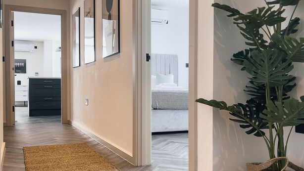 A hallway with a woven rug, a potted plant, and framed pictures on the wall. - Luxe Penthouse Retreat: With Free Parking! (London)