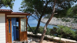 Eine Holzhütte mit Glastür, einer kleinen Veranda und Blick auf das Meer und die felsige Küste.