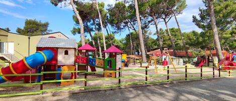 A playground with various play structures, surrounded by trees and buildings.