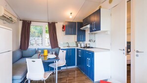 Una cocina compacta con armarios azules, una mesa de comedor con sillas blancas, una estufa empotrada y una ventana con cortinas.