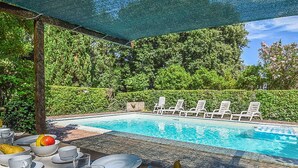 Un espace repas aménagé au bord de la piscine, avec une table dressée pour deux personnes, entourée de chaises longues.