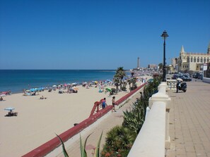 Stroll along the promenade, lined with palm trees and a historic building with a pointed roof and lighthouse in the background.