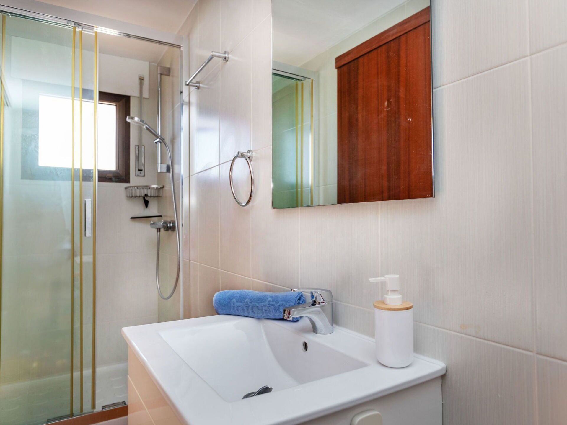 A bathroom with a glass shower enclosure, a white sink with a blue towel, and a wooden cabinet above the mirror.