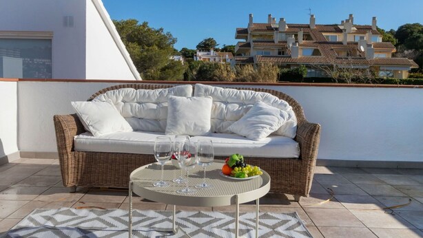 A balcony with a wicker sofa, a round table with glasses and fruit, and a patterned rug. - Cosy apartment for 6 people with WIFI, pool, TV and terrace (Castell-platja D'aro)
