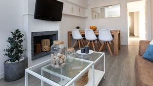 A modern living room with a glass coffee table, a flat-screen TV mounted on the wall, a fireplace, and a dining area with a wooden table and white chairs. - Cosy apartment for 6 people with WIFI, pool, TV and terrace (Castell-platja D'aro)