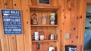 Ein Holzblockhaus-Innenraum mit einer Kaffeestation, einem Schild für Freizeitaktivitäten am See und einem Hundeschild darüber.