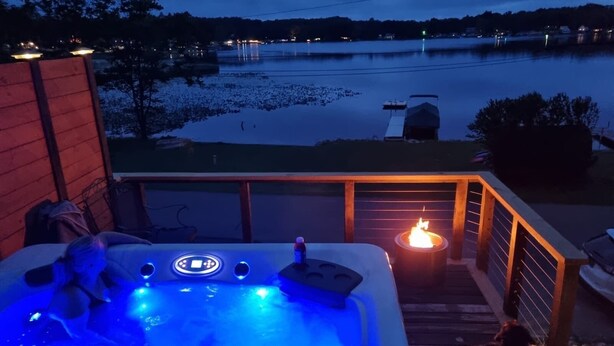 Ein Whirlpool mit einer Holzterrasse und Blick auf einen See im Abendlicht.