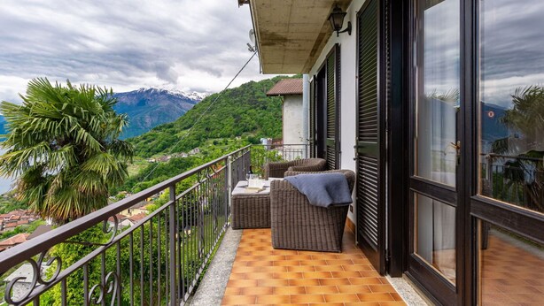 En balkon med udsigt over et bjergrigt landskab, en fletningssofa og flisegulv.