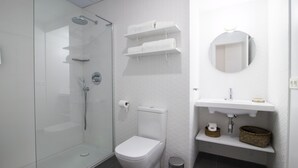 Ein modernes Badezimmer mit einer gläsernen Duschkabine, einer weißen Toilette und einem Waschbecken mit Spiegel darüber. Über dem Waschbecken befinden sich Regale für Handtücher und ein Mülleimer neben der Toilette.