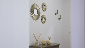 Eine Wand mit drei dekorativen Spiegeln und zwei Wandleuchten. Darunter ein Holzschrank mit einer Vase und Schilfhalmen sowie zwei kugelförmigen Objekten.