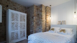 Ein Schlafzimmer mit Backsteinwand, einem großen weißen Kleiderschrank, einem Bett mit weißer Bettwäsche und einer hängenden Glühbirne.