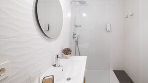 Une salle de bain moderne avec un meuble-lavabo blanc, un grand miroir, un espace douche et une petite plante en pot posée sur le lavabo.